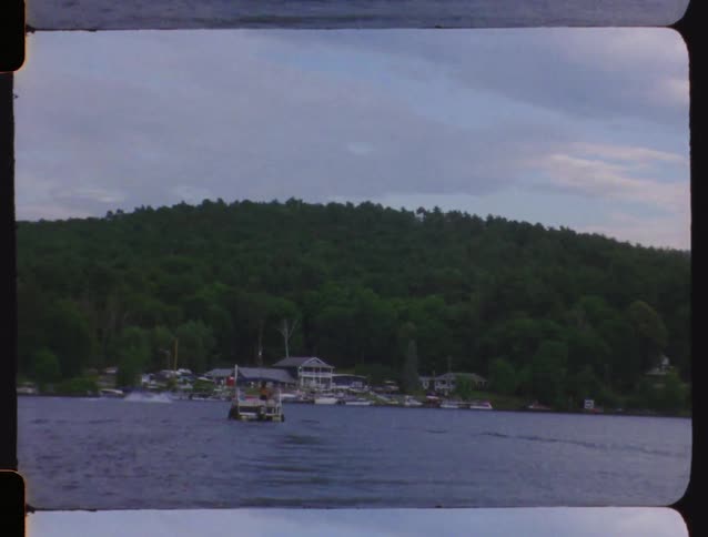 Vintage Super 8 film captures a tranquil boat ride on a lake towards a lush, tree-covered shoreline