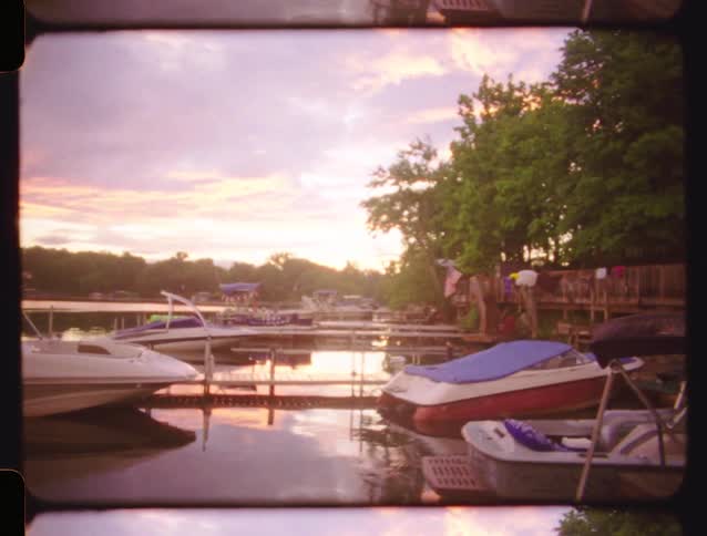 Vintage footage of a serene lake at sunset pans right to reveal boats tied up at a quiet marina