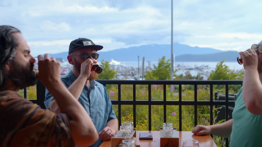 Friends cheers and enjoy a flight of craft beer on a scenic brewery patio overlooking a beautiful marina