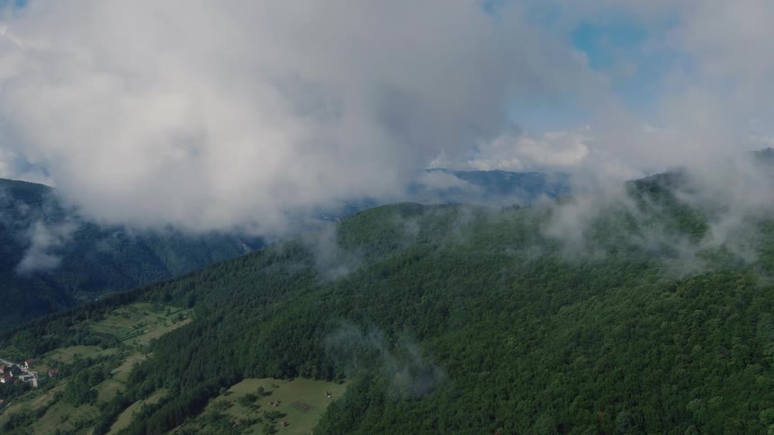 An atmospheric aerial view shows a slow forward flight over verdant mountain forests partially hidden by ethereal fog