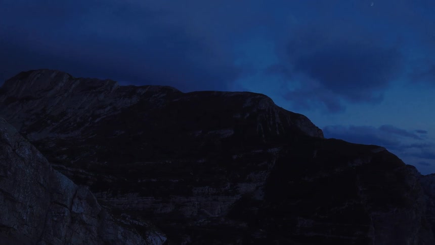 A slow zoom reveals the silhouette of a mountain range under a crescent moon in the dark blue night sky