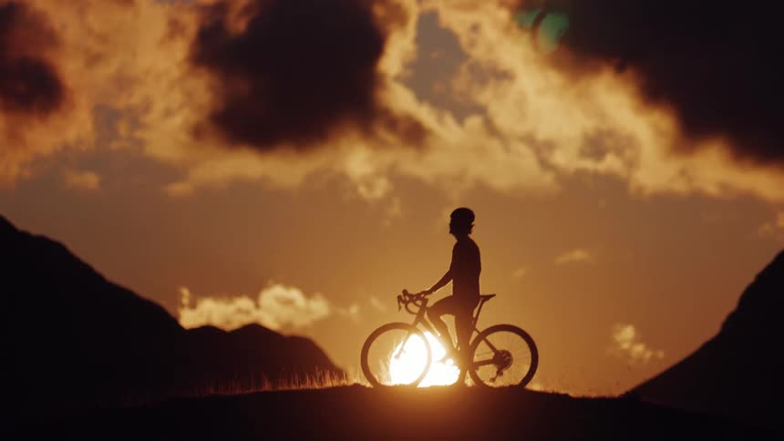 A lone cyclist stops on a mountain ridge to enjoy the breathtaking golden hour sunset