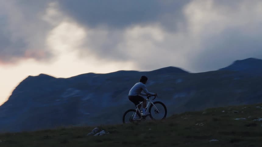A cyclist pedals along a scenic mountain trail at twilight, but the challenging terrain causes them to fall