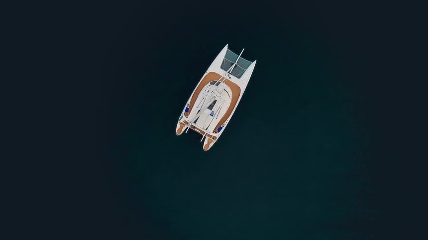 An aerial top-down view of a single white catamaran boat floating peacefully in the dark blue ocean