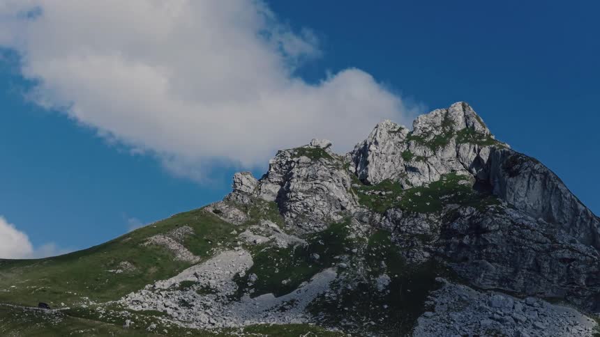 A time-lapse view of a rugged mountain peak with clouds drifting by in the bright blue sky