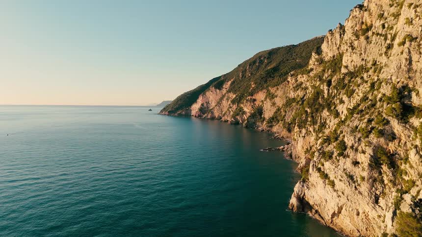 Aerial view of a rugged, sun-kissed coastline with steep cliffs descending into the tranquil blue ocean at golden hour