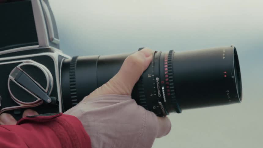 A photographer manually adjusts the focus ring on a large vintage camera lens