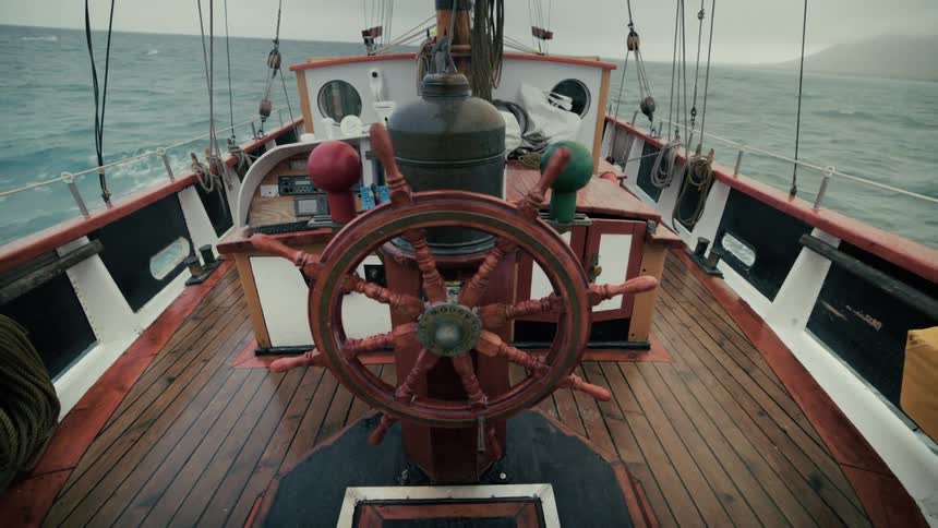 A historic wooden sailing ship rocks back and forth on the choppy sea during a storm