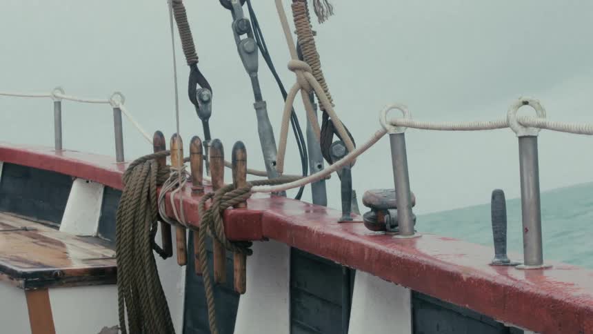 Close-up of a sailboat's wet railing and rigging while sailing on a choppy sea during an overcast day