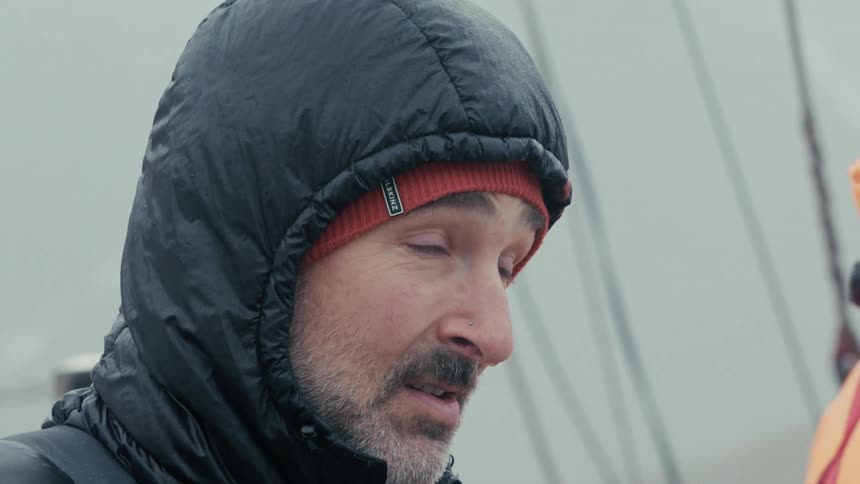A slow-motion close-up of a thoughtful man wearing a hooded winter jacket and red beanie on an overcast day