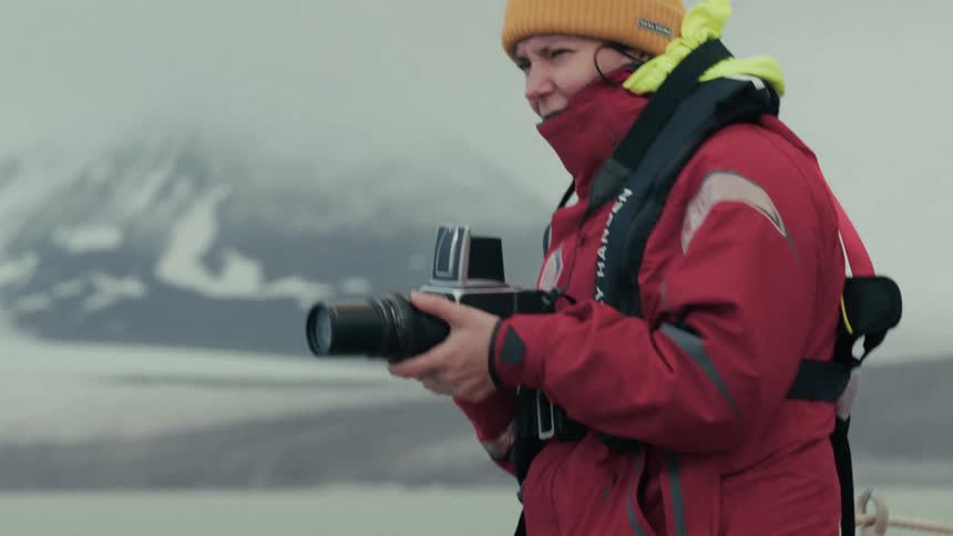 A photographer bundled in warm clothing captures photos of a snowy arctic landscape from a boat