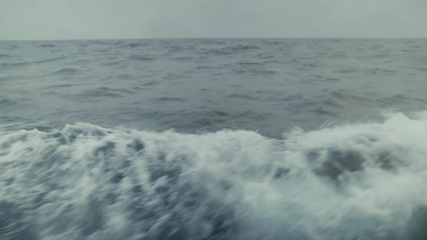 The foamy wake of a boat cuts through the vast, grey ocean on an overcast day