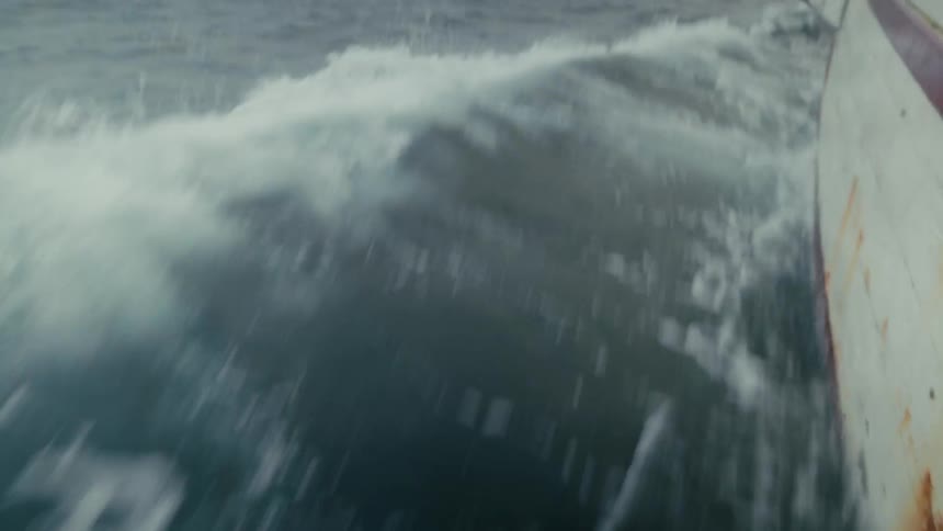 A view from the side of a boat as it cuts through the choppy gray ocean waters on a foggy day