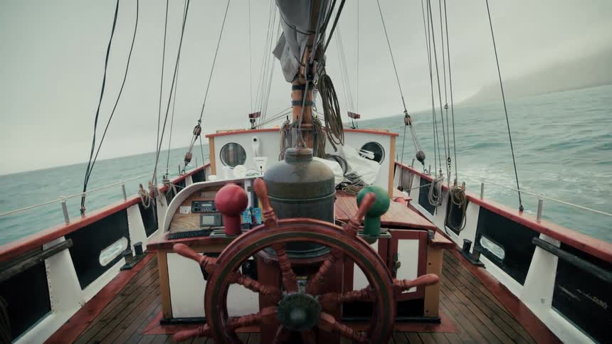 View from the helm of a vintage wooden sailboat sailing on the rough sea on a foggy day