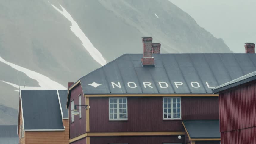 A close up of the Nordpol hotel in Ny-Ålesund, Svalbard, with snow-covered mountains in the background on an overcast day