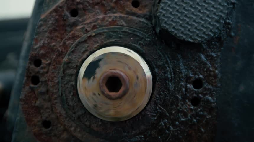 Extreme close-up of a rusted industrial hex bolt spinning rapidly on old, greasy machinery before coming to a sudden stop