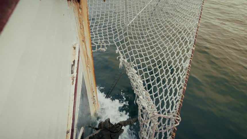 A high-angle rack focus shot reveals the bow of an old boat sailing steadily through the ocean