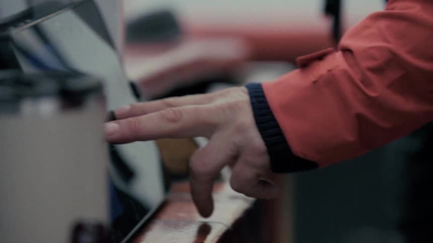 Close-up of a person's hands using a touch screen tablet while wearing an orange rain jacket