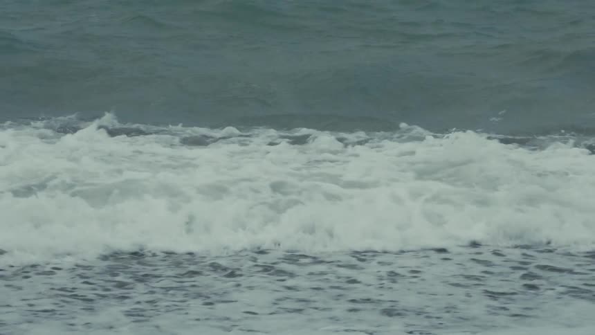 A powerful ocean wave crashes onto a rocky shore in dramatic slow motion on a stormy day