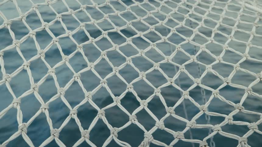 Calm blue ocean waves move rhythmically beneath a white rope net on a boat