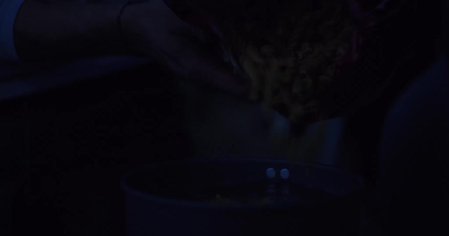 A close-up slow-motion shot of pouring dry fusilli pasta into a pot of water in a dark kitchen