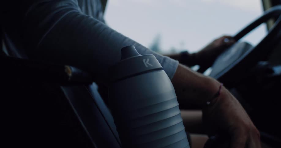 A reusable water bottle sits in the center console of a car as a person drives down a road