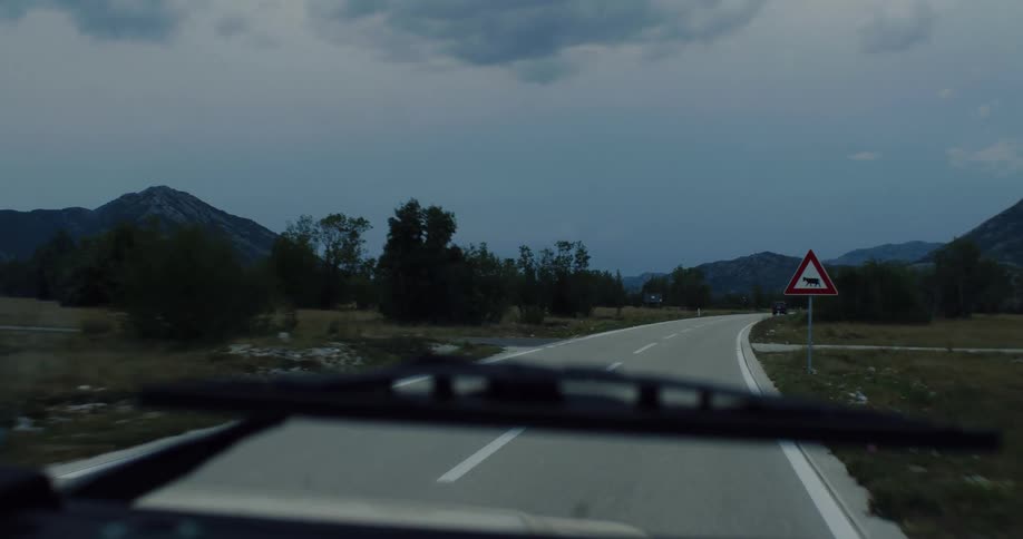 Driving a car on a remote road through a mountain valley at twilight under dramatic, stormy clouds