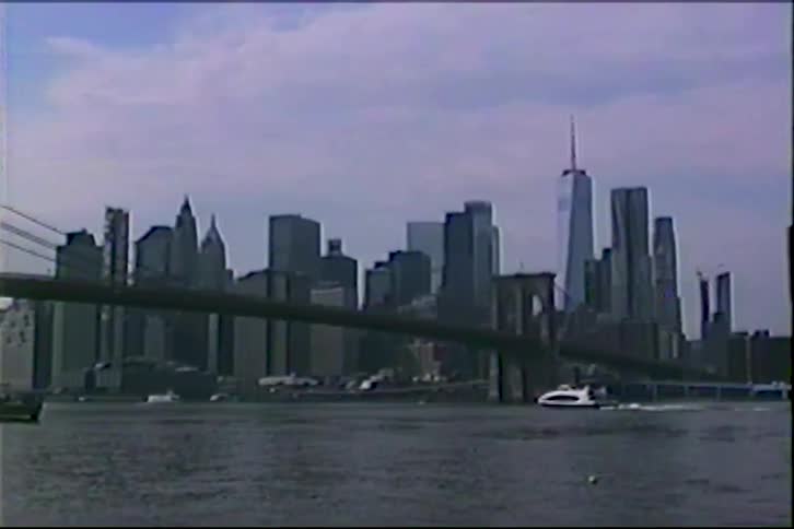 A retro VHS-style shot captures the iconic Lower Manhattan skyline with the Brooklyn Bridge and a ferry crossing the East River