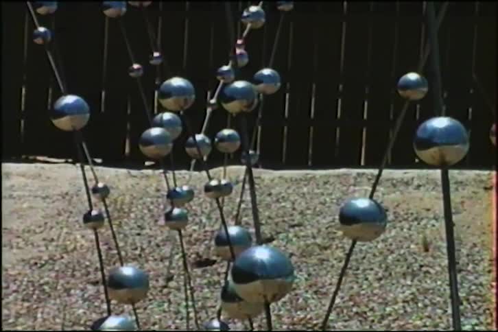 Vintage footage tilts up on an abstract metal sphere sculpture in a desert garden with mountains in the background