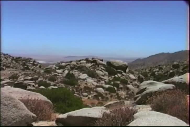 Vintage VHS footage captures a static wide shot of a rocky, arid mountain pass under a clear blue sky