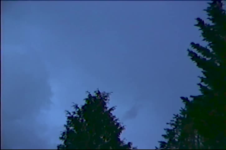 Lightning flashes across a dark, stormy night sky above silhouetted trees in vintage footage