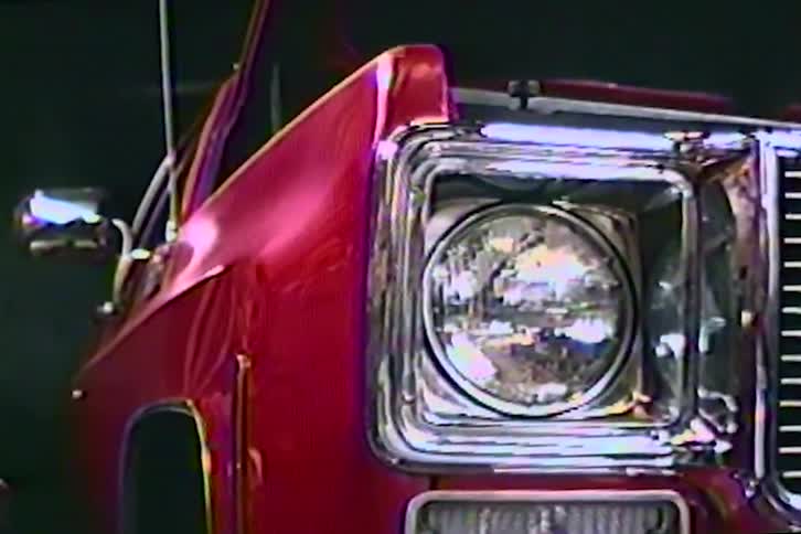 A retro VHS close-up of a shiny red classic American truck's chrome headlight