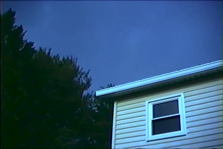 A bright purple lightning bolt flashes across the dark night sky above a house during a thunderstorm