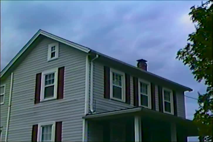 Vintage VHS footage zooms in on a classic two-story suburban home under an overcast sky
