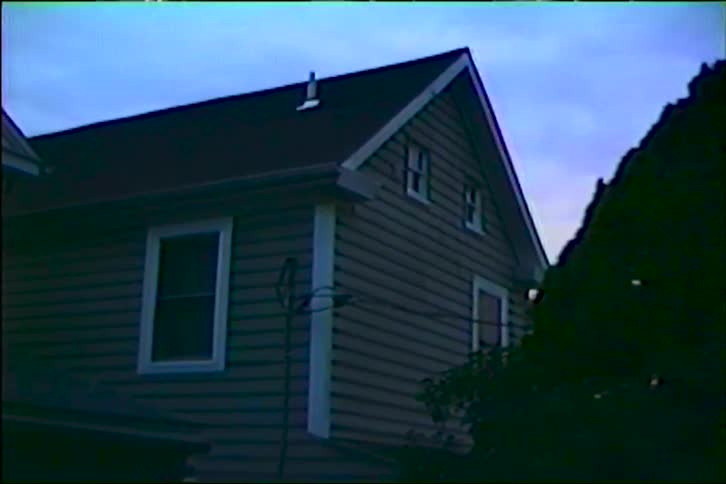 Vintage VHS footage captures a static view of a suburban house against the deep blue twilight sky