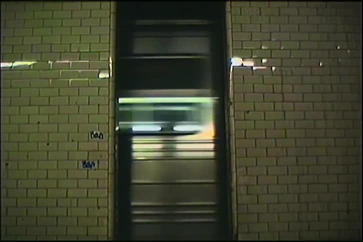 Archival shot of a subway train speeding through a station, seen between the cars as a blur of lights and motion