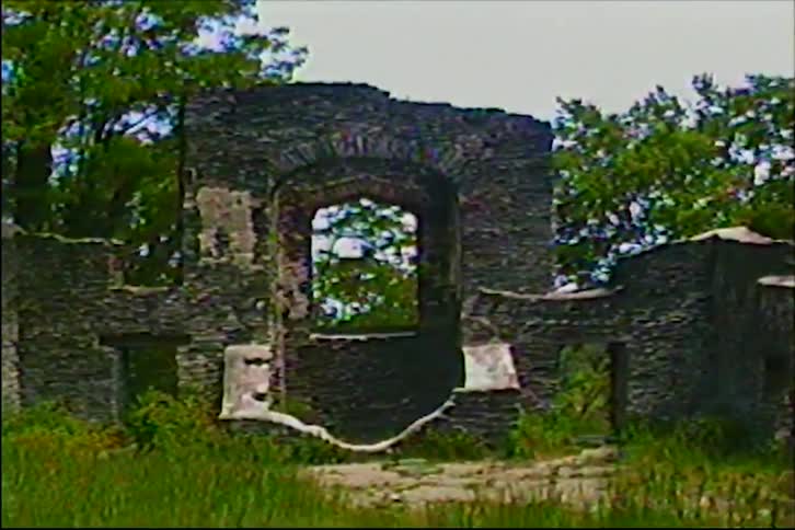 Vintage VHS footage zooms out from a leafy treetop view to reveal ancient, overgrown stone ruins in a forest