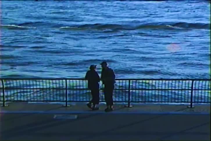 A silhouetted couple shares an intimate conversation and a kiss on a pier overlooking the choppy ocean waves