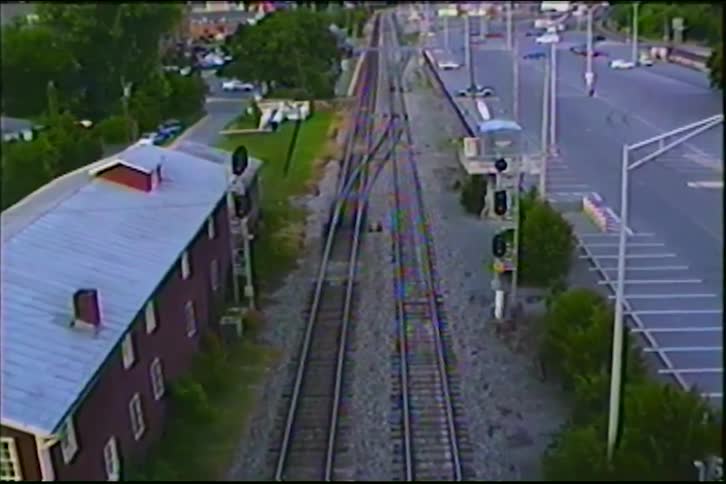 A high-angle, static shot from vintage footage shows empty railroad tracks running through a quiet town