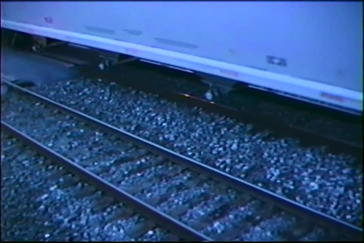 A high-angle close-up of a freight train's wheels moving along a gravel railroad track