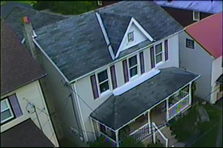 Vintage VHS footage shows an aerial view slowly zooming in on a small cat sitting in the window of a suburban home