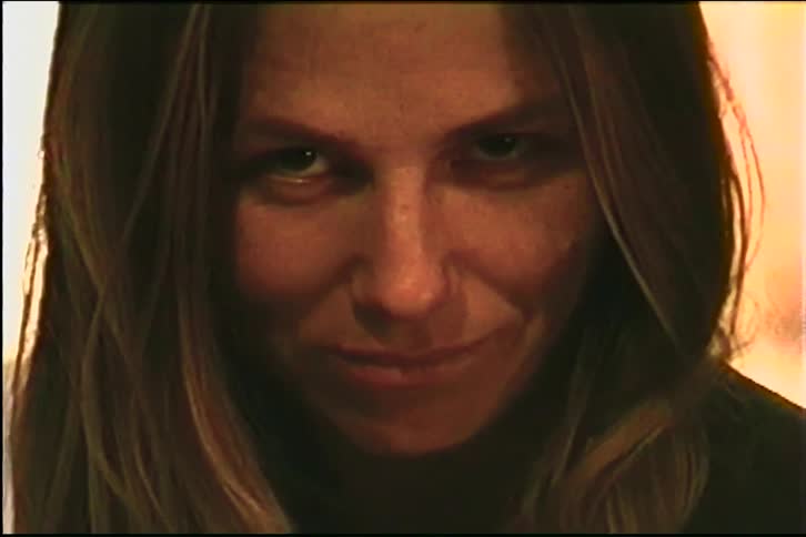 An eerie close-up of a woman with a sinister smile and intense stare, with VHS tape glitches and distortion