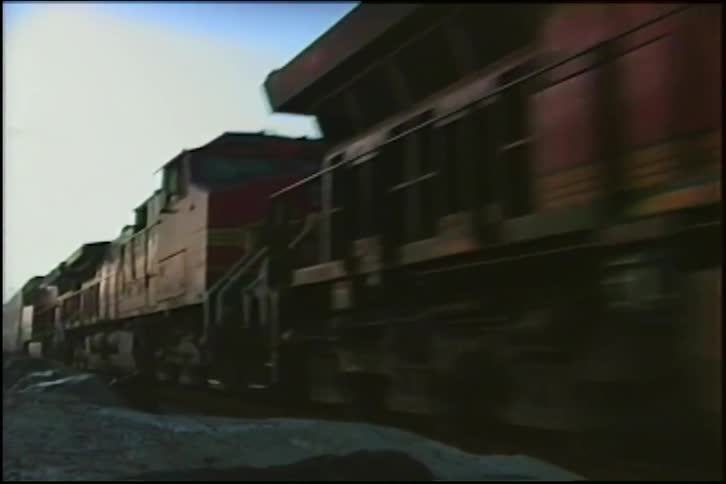 A low-angle view of a red Santa Fe freight train passing by on coastal tracks with its headlights on at dusk