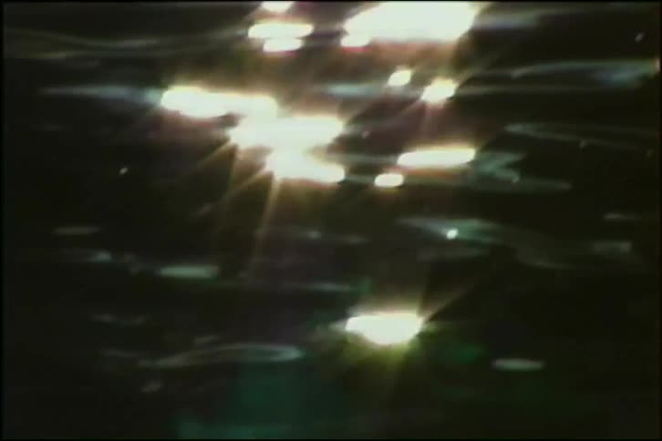 Abstract close-up shot of shimmering sunlight reflections sparkling on the surface of dark, rippling water
