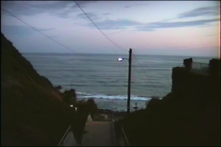 A vintage VHS shot captures the serene view down a coastal stairway to the ocean at dusk