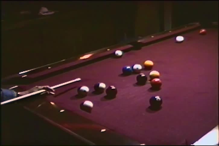 Vintage footage captures a player sinking a striped ball into the corner pocket during a game of pool on a purple table