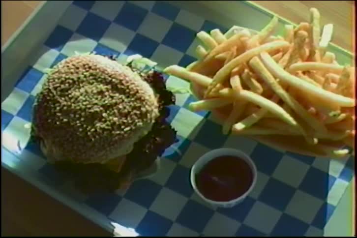 A slow zoom in on a hamburger and french fries meal sitting on a tray with a blue and white checkered liner