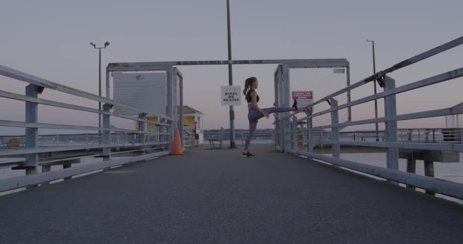 Woman stretches leg on a railing near water