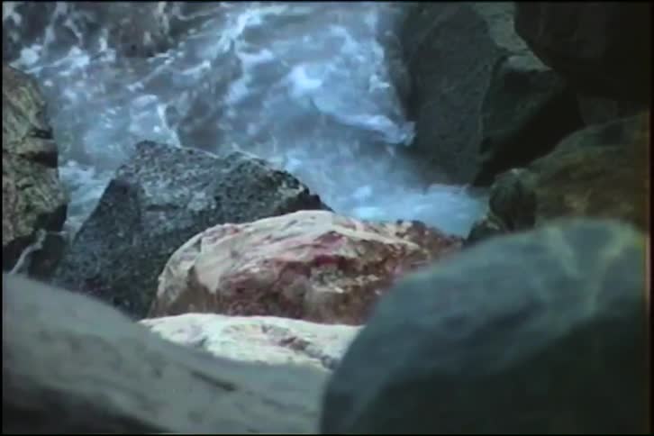A close-up, vintage-style shot captures the turbulent flow of foamy water crashing against large rocks