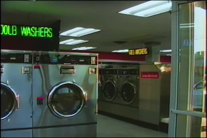 A slow pan across rows of industrial washing machines inside a vintage, empty laundromat